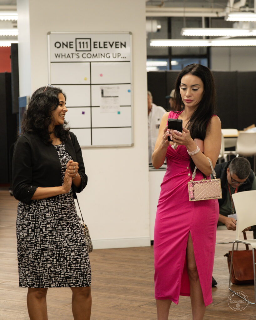 Two attendees connect beside the OneEleven welcome board at the AI & Film Forum.