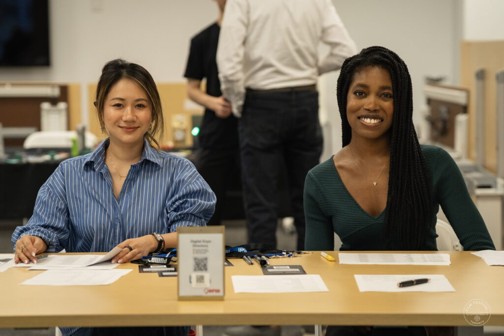 Two smiling event team members welcome attendees at the AI & Film Forum registration desk.