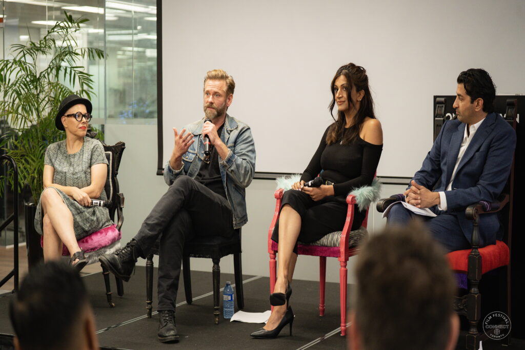 Four panel participants sit on stage as one speaks into a microphone and gestures to the audience.