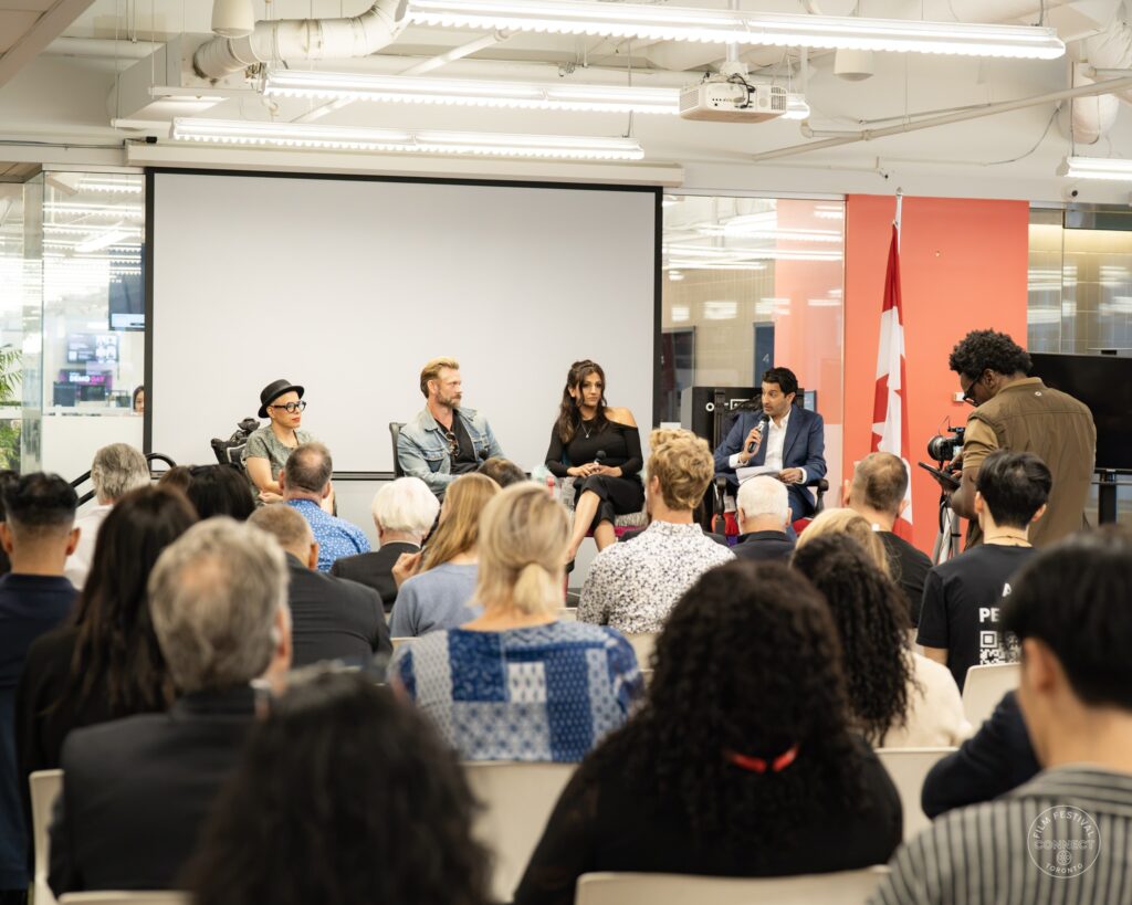 An audience faces four seated panel participants, with a camera operator beside the stage. AI & Film Forum, Panel 1, September 14, 2026.