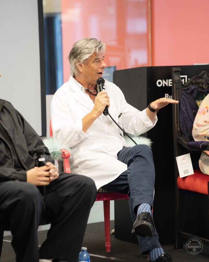 A panel participant in a white coat speaks into a microphone and gestures with his free hand. AI & Film Forum, Panel 2, September 14, 2026.