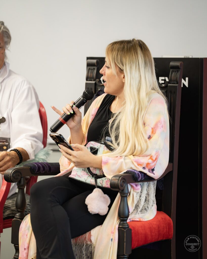 A panel participant wearing a patterned shawl speaks into a microphone and gestures toward the other speakers. AI & Film Forum, Panel 2, September 14, 2026.