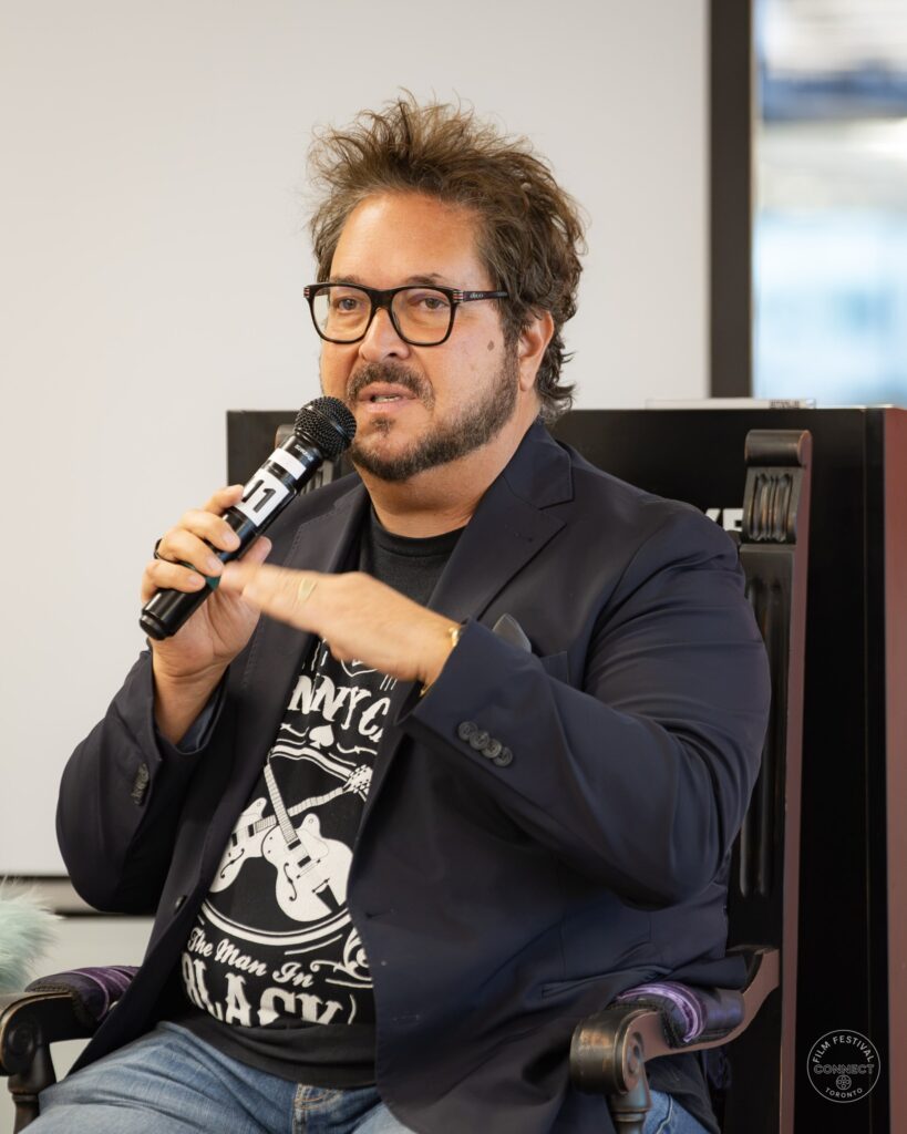 A panel participant in a dark blazer speaks into a microphone and gestures with his other hand. AI & Film Forum, Panel 3, September 14, 2026.