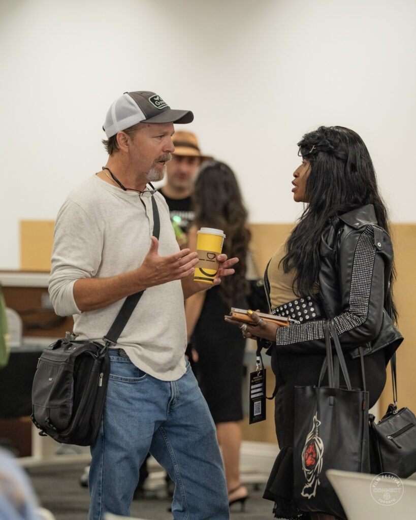 An attendee in a grey cap chats with a woman in a black jacket at the AI & Film Forum.