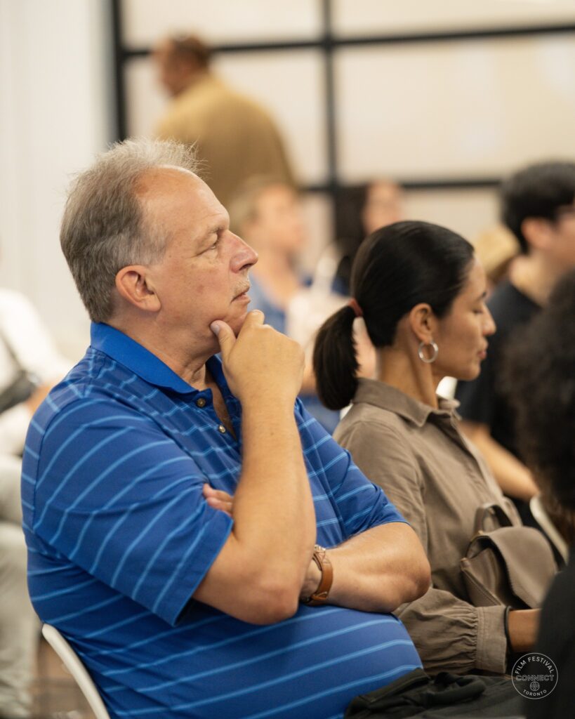 A seated attendee in a blue striped shirt listens thoughtfully at the AI & Film Forum.